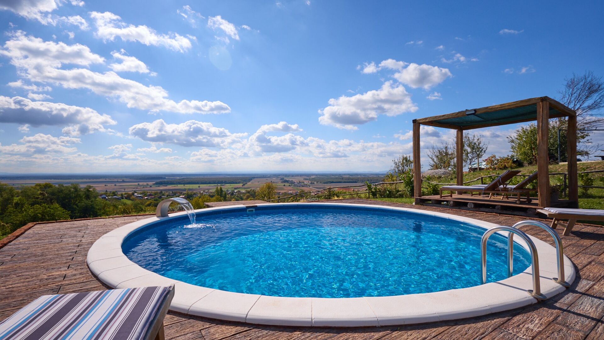 Une piscine avec une terrasse en bois, des chaises longues et une pergola.