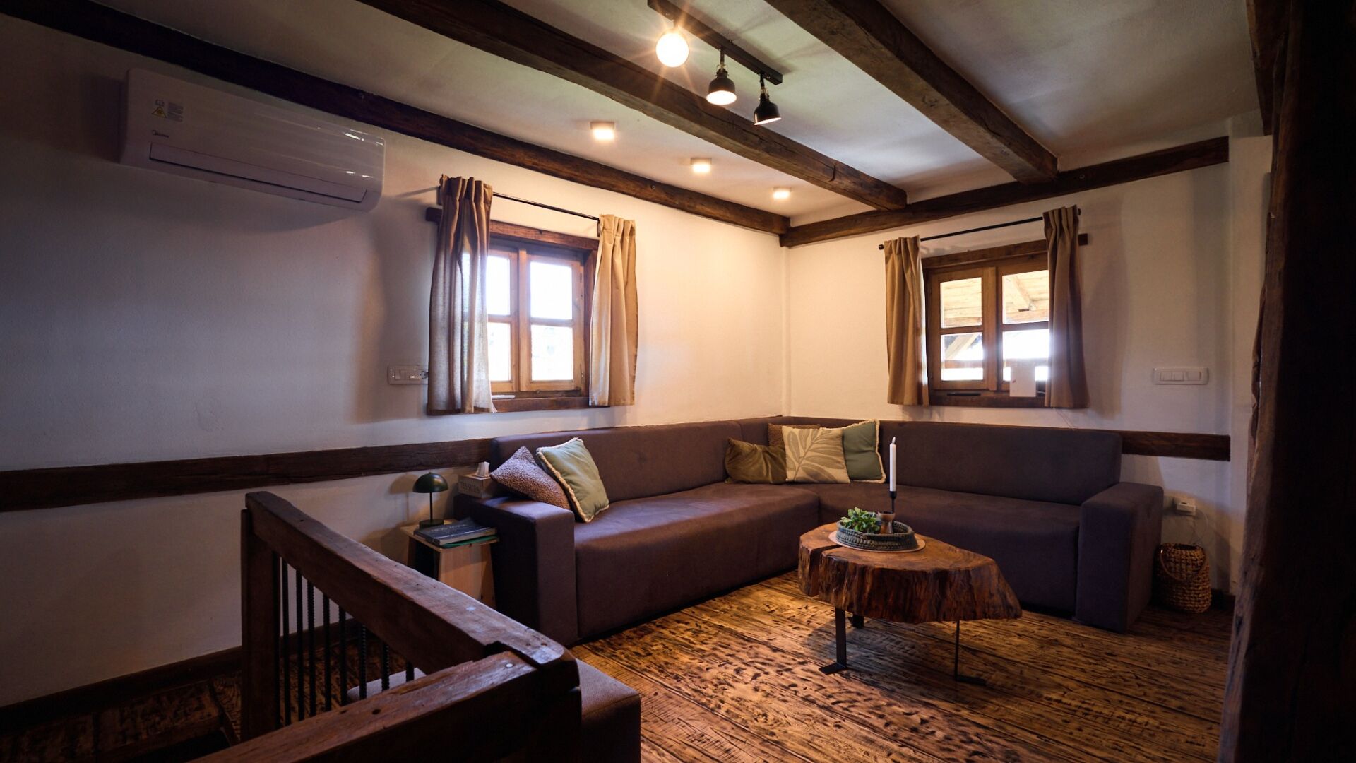 A cozy room with a wooden floor, a brown sofa, a small wooden table, and a staircase.