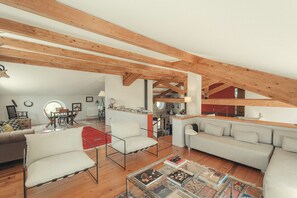 A spacious loft with exposed wooden beams, a dining area, a living room with a sofa and chairs, and a kitchen area.