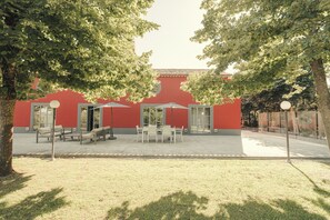 A red building with a patio area featuring tables and chairs, surrounded by trees.