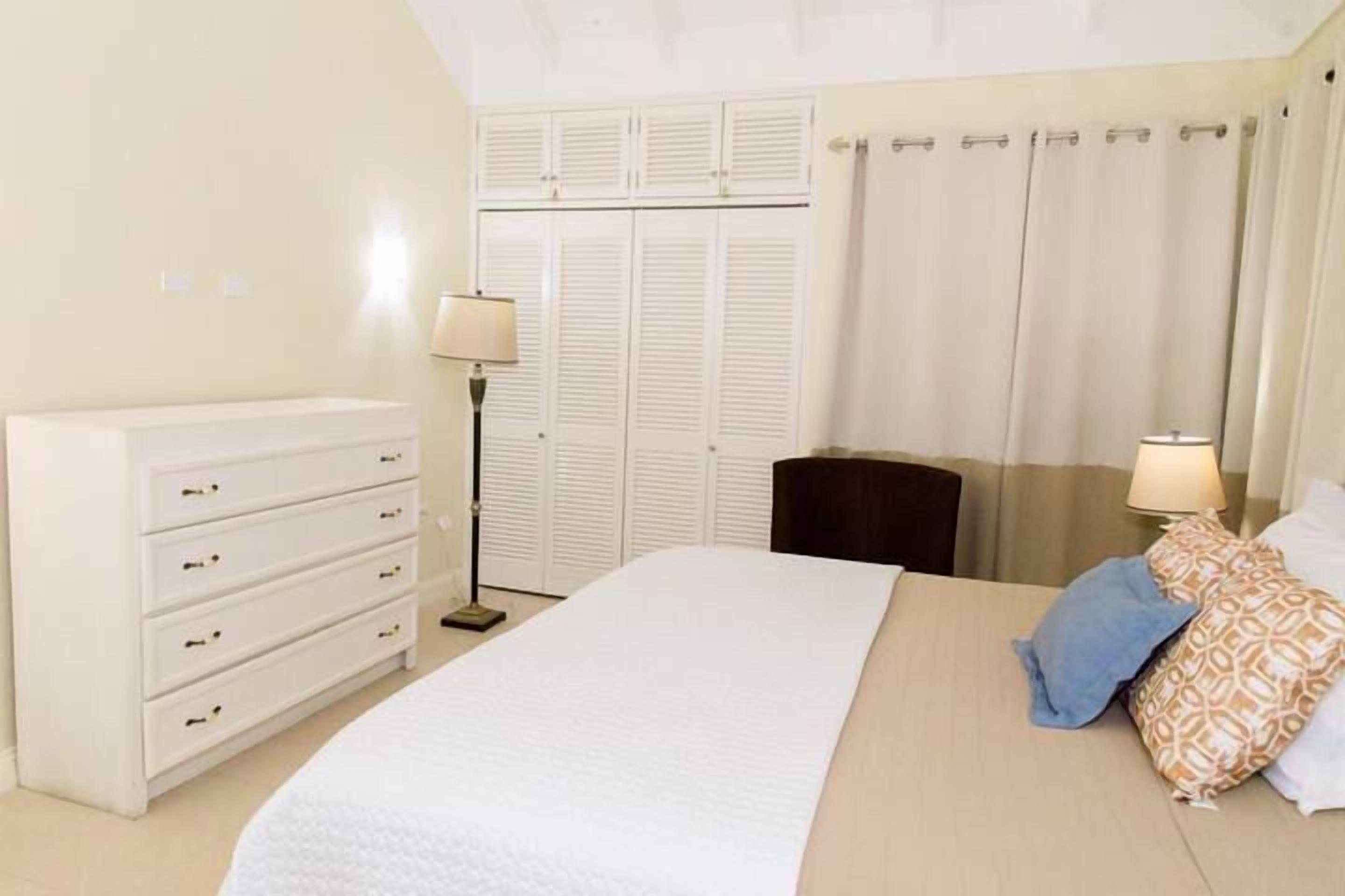 Un dormitorio con cama, cómoda, lámpara, armario y cortinas.