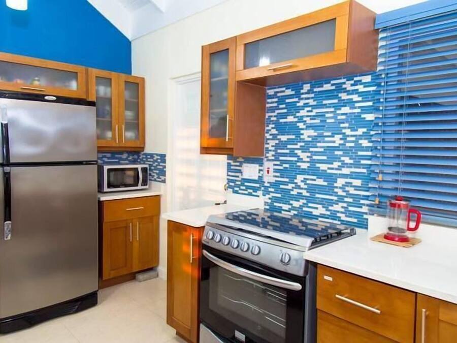 A modern kitchen with wooden cabinets, a stainless steel refrigerator, a microwave, a stove, and a tiled backsplash.