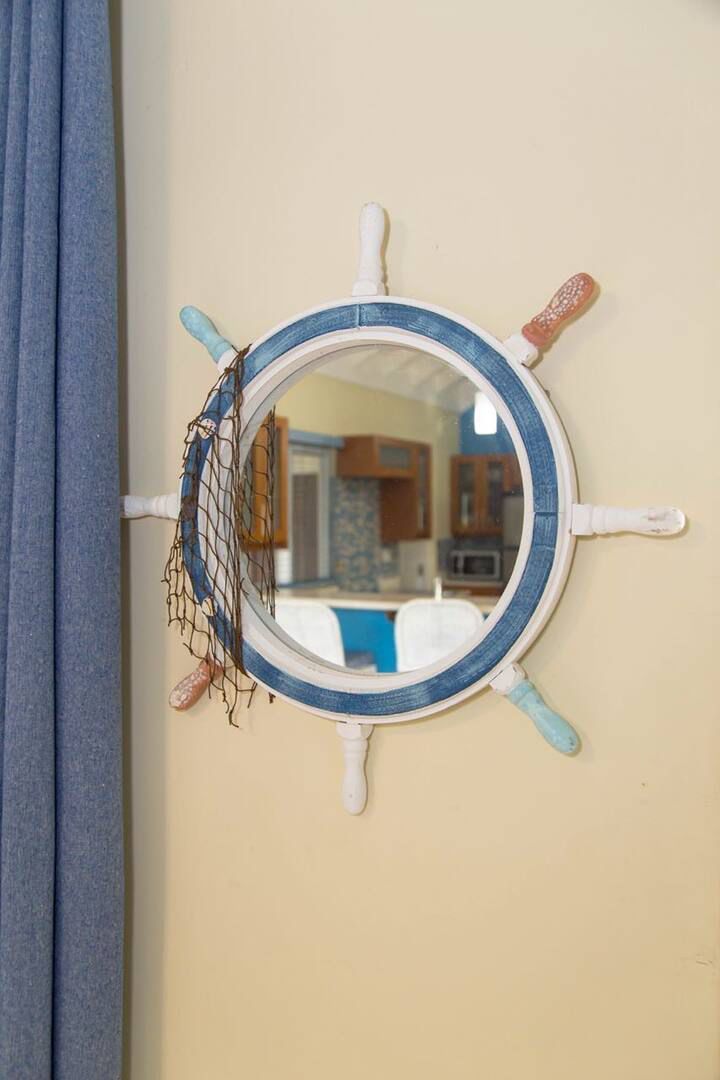 Een rond spiegel aan de muur met een roer ontwerp, inclusief touw en een klein figuur dat aan het roer hangt.