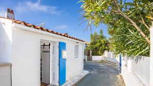 Une rue étroite mène à un bâtiment blanc avec une porte bleue, un toit recouvert de tuiles et un mur blanc.