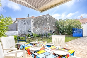 Une terrasse extérieure avec une table dressée pour le repas, des chaises, un espace salon abrité et des vélos en arrière-plan.
