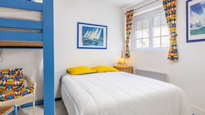 Une chambre à coucher avec un lit, une chaise, un tableau, une fenêtre avec des rideaux et une table de chevet avec une lampe.