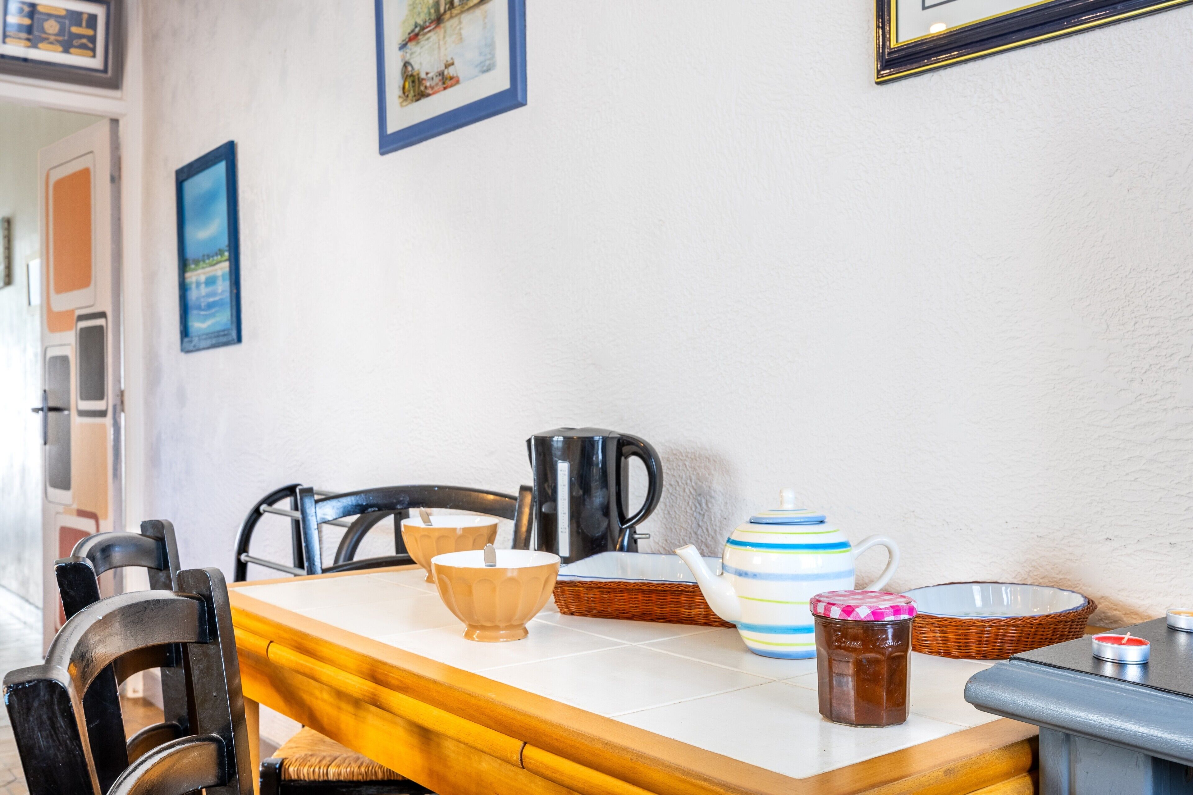 Una mesa de comedor con sillas, una tetera, un cesto, un bol y una vela.