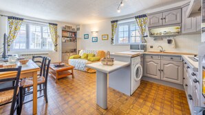 Une cuisine compacte équipée d’un lave-linge, un coin repas avec des chaises et une table, et un canapé avec des coussins.