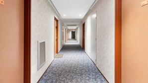 A hotel hallway with a patterned carpet, wooden doors, and a vent on the wall. - Apartment 'L'aventurier' – Steps from Futuroscope, Sleeps 4 (chasseneuil du Poitou)