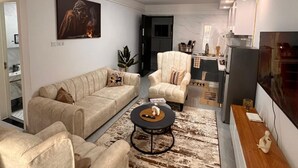 A living room with a beige sofa, armchair, and coffee table. There is a painting on the wall and a plant in the corner. - Modern kilimani stay in the heart of Nairobi (Nairobi)