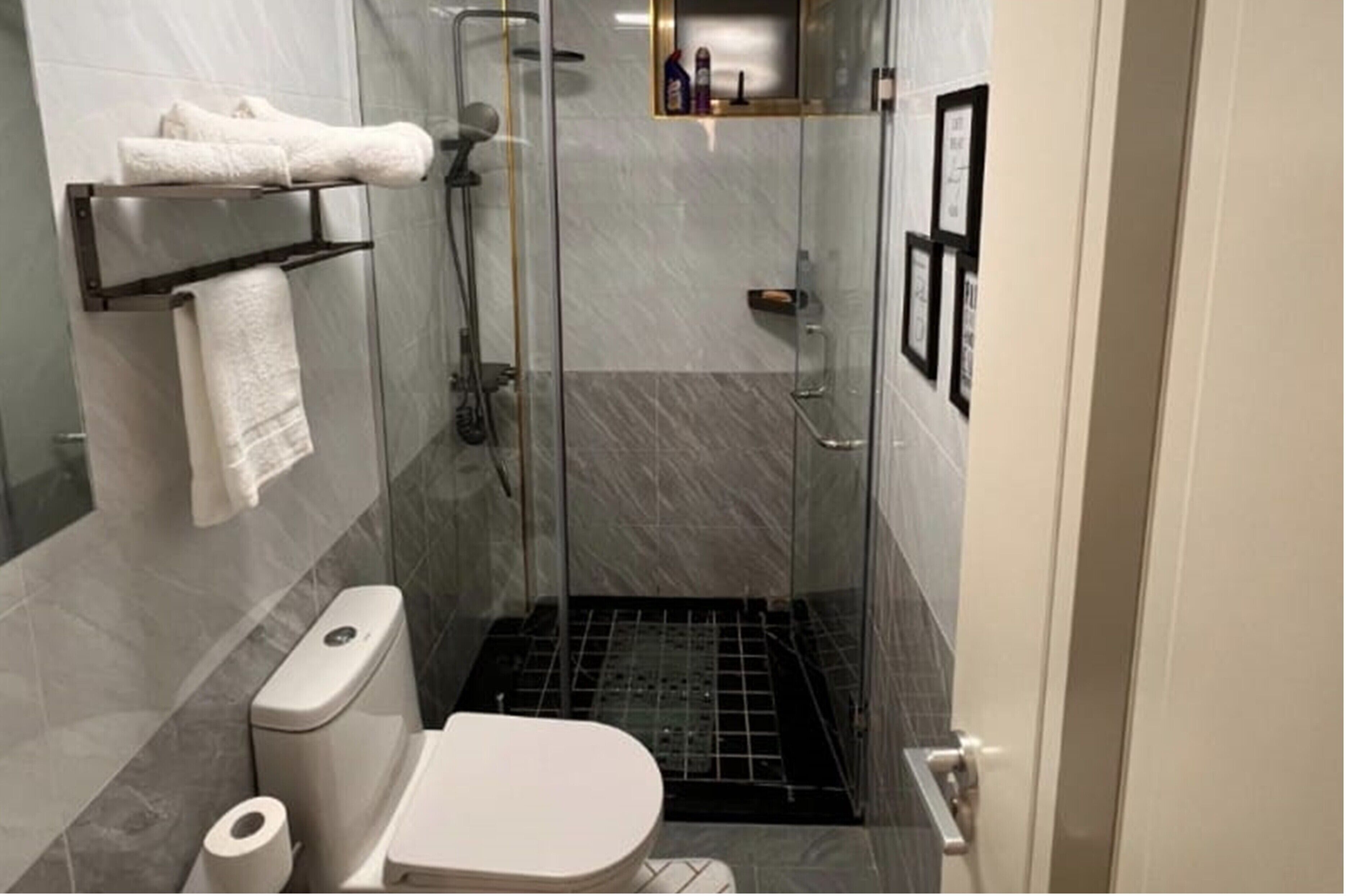 Une salle de bain moderne avec une douche à parois de verre, des toilettes, un porte-serviettes et une petite étagère contenant des articles de toilette.