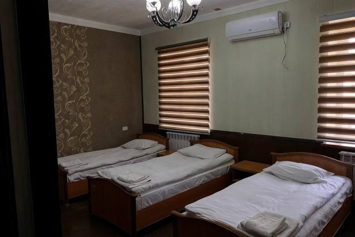 Una habitación con tres camas individuales, un radiador y una ventana con persianas.
