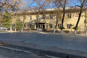 A building with a central entrance, multiple windows, and a fenced area with trees. - N&J Hotel-Process equipment only (Jizzakh District)