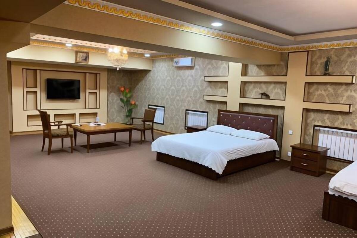 Habitación de hotel con cama, escritorio, sillas, televisor y estanterías.
