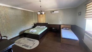 A bedroom with a bed, a desk, and a chair. There is a window with blinds and a radiator.