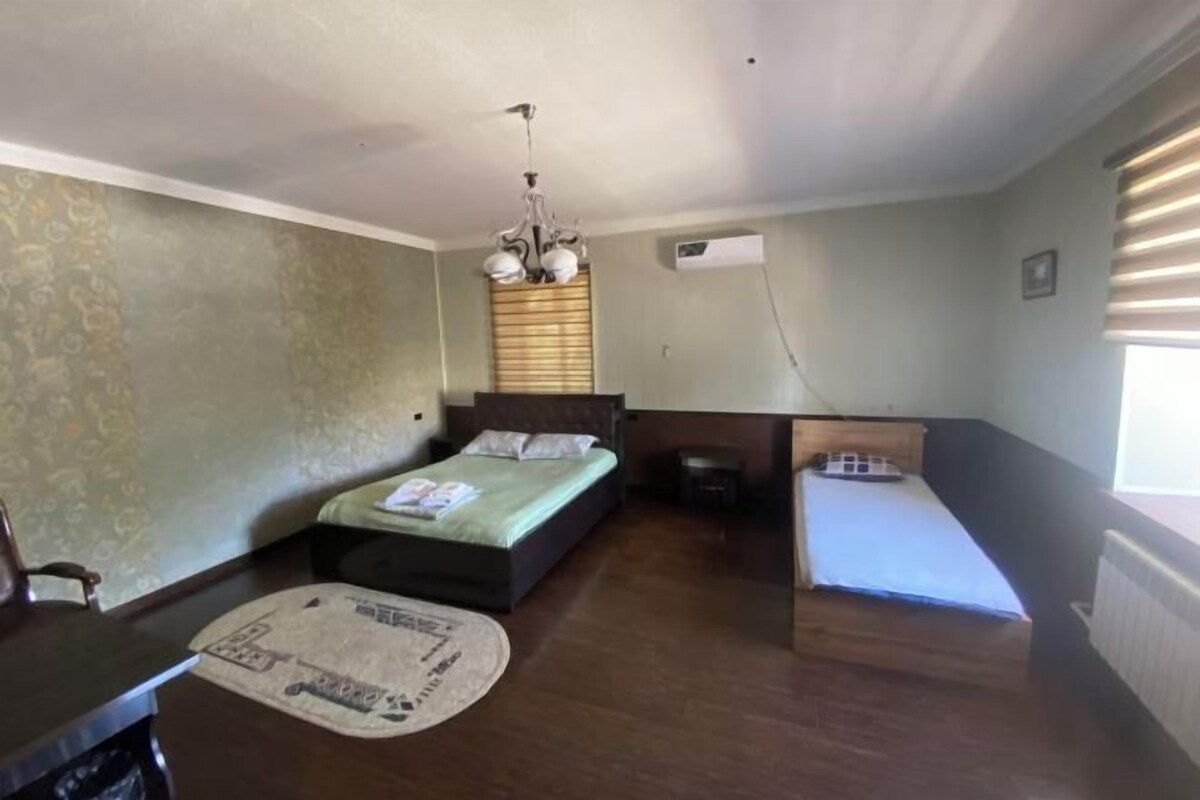 A bedroom with a bed, a desk, and a chair. There is a window with blinds and a radiator.