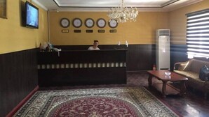 A reception area with a reception desk, a chandelier, a clock, and a television on the wall. - N&J Hotel-Process equipment only (Jizzakh District)
