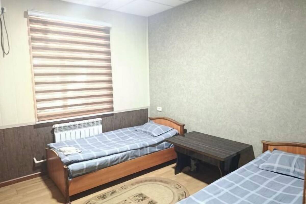 Una habitación con dos camas, una mesita, un radiador y una ventana con persianas.