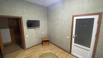 A room with a wooden floor, a television mounted on the wall, a small wooden cabinet, and a door with frosted glass.