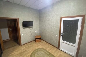 A room with a wooden floor, a television mounted on the wall, a small wooden cabinet, and a door with frosted glass. - N&J Hotel-Process equipment only (Jizzakh District)