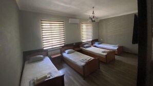 A room with three single beds, a chandelier, and two windows with blinds.