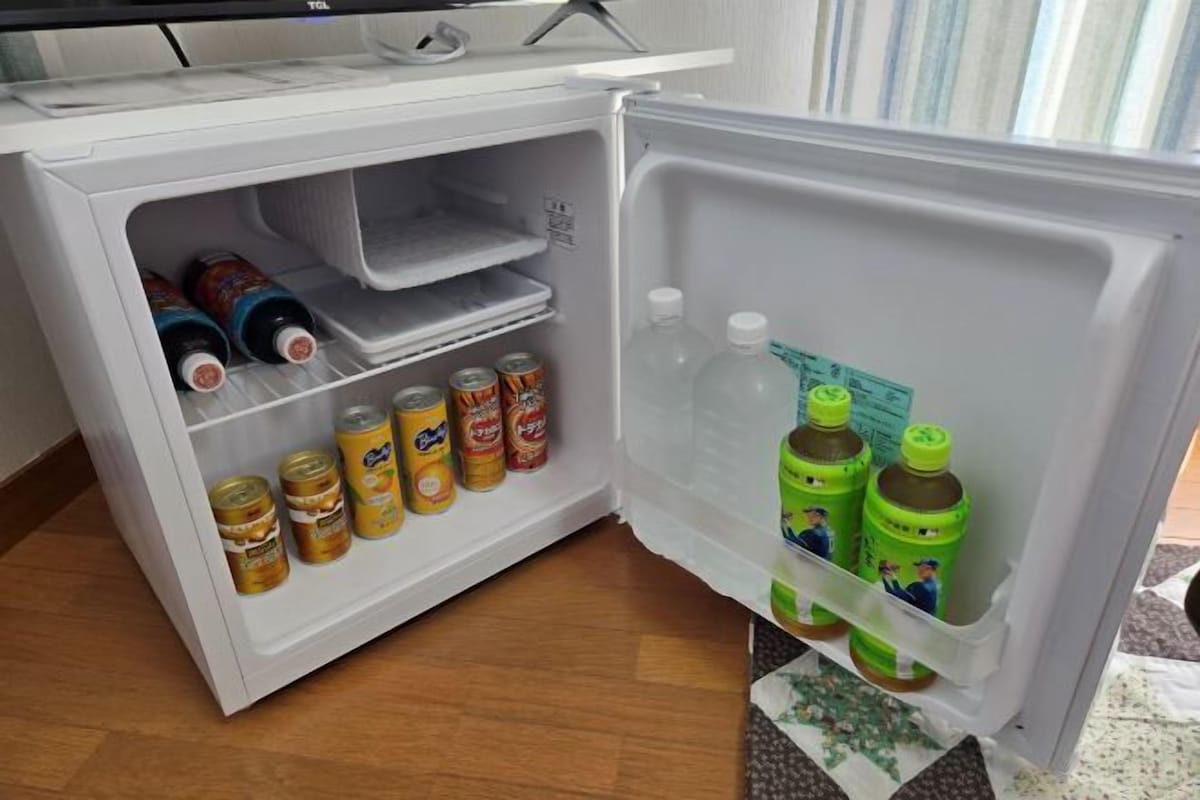 A small white refrigerator with a TV on top, containing various beverages and condiments.