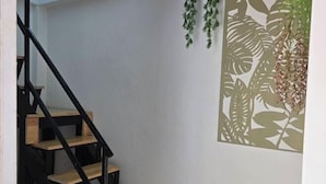 A staircase with wooden steps and black railings, leading to a room with a white wall and a decorative plant hanging from the ceiling. - Manonkan Kranuan (Kranuan)