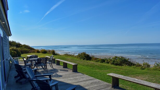 Una terraza de madera con mobiliario exterior, con vistas a una playa y al océano.