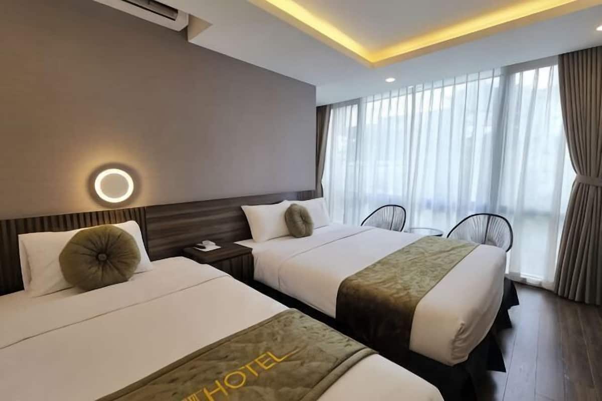 A hotel room with two beds, a bedside table, a lamp, a chair, and a large window with curtains.
