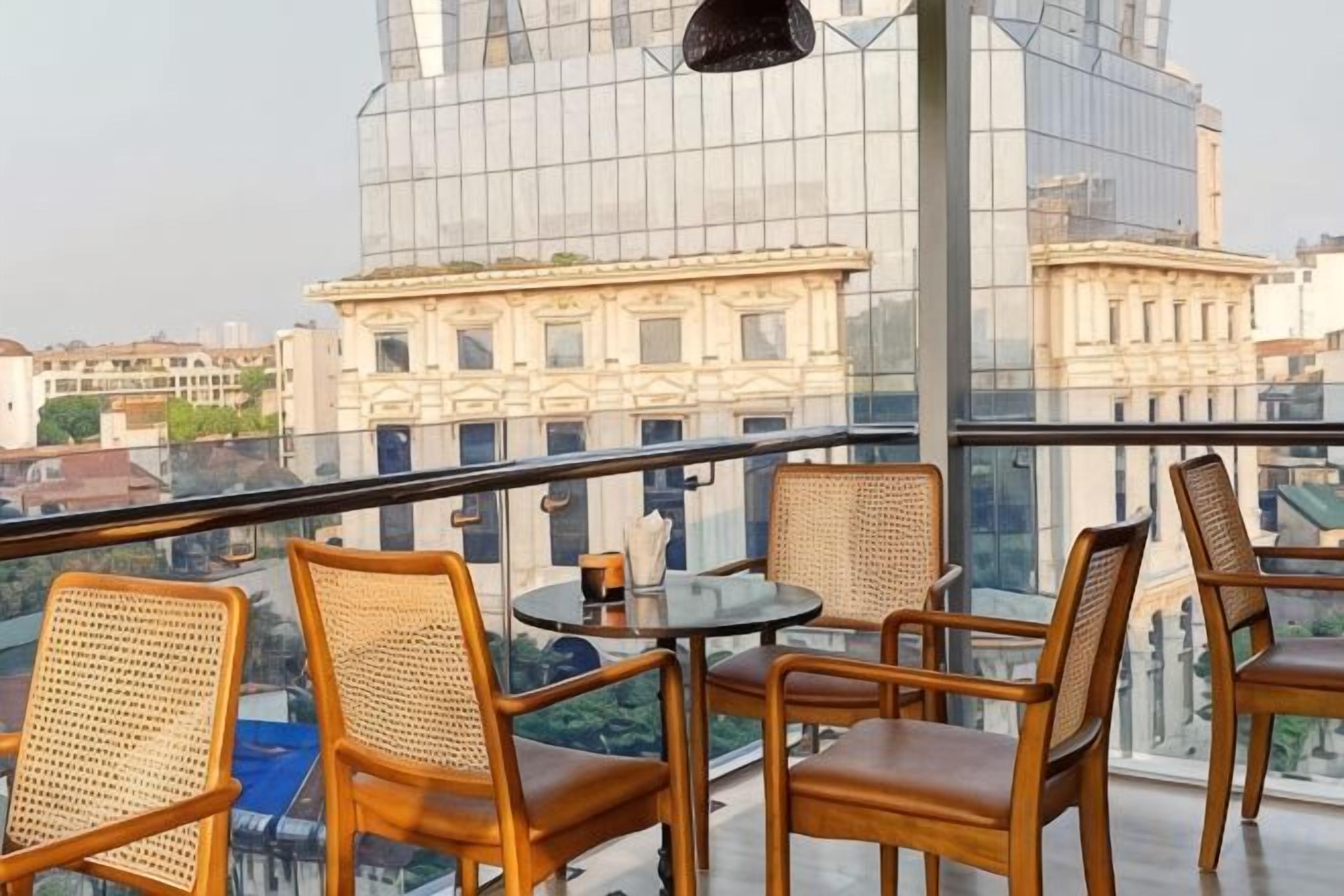 Ein Balkon mit Korbstühlen und einem kleinen Tisch, mit Blick auf eine Stadtlandschaft mit klassischer Architektur.