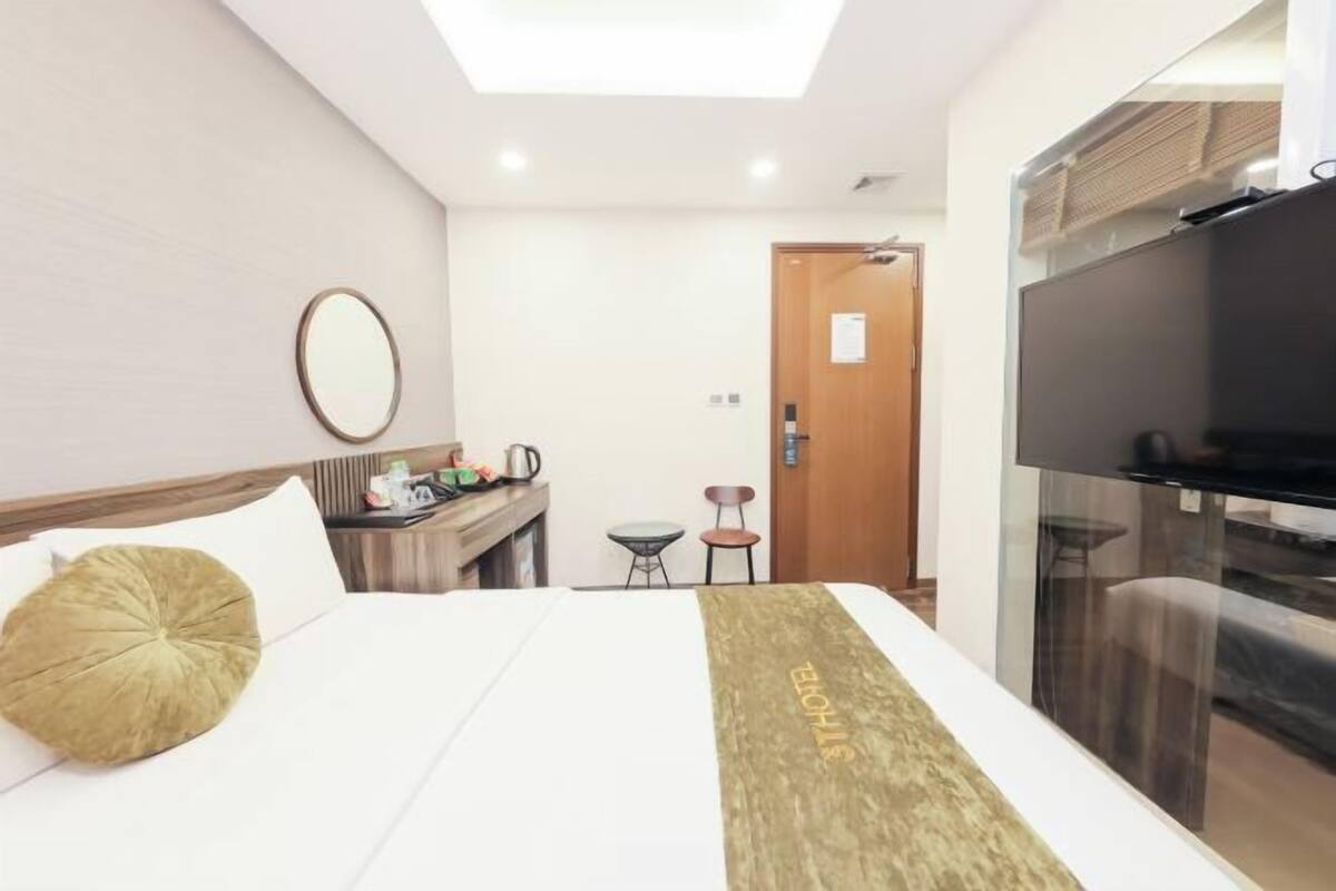 A hotel room with a bed, a desk with a chair, a TV, and a door.