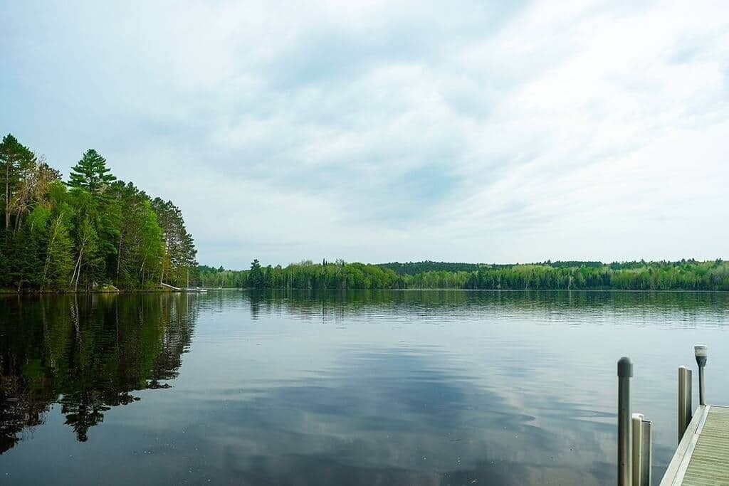 Un lago tranquillo con un pontile che si protende nell'acqua, circondato da una fitta foresta.