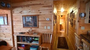 Ein Holzblockhaus-Innenraum mit Bücherregal, gerahmtem Bild und Holzstuhl.
