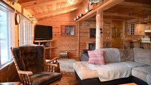 Ein gemütliches Blockhaus-Interieur mit Holzbalkendecke, einem Fernseher, einer Couch und einem Essbereich.