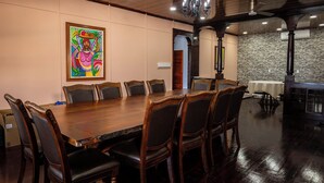 A conference room with a long wooden table and chairs, a chandelier, and a stone wall. - The Ambassador's Terrace (Belize City)