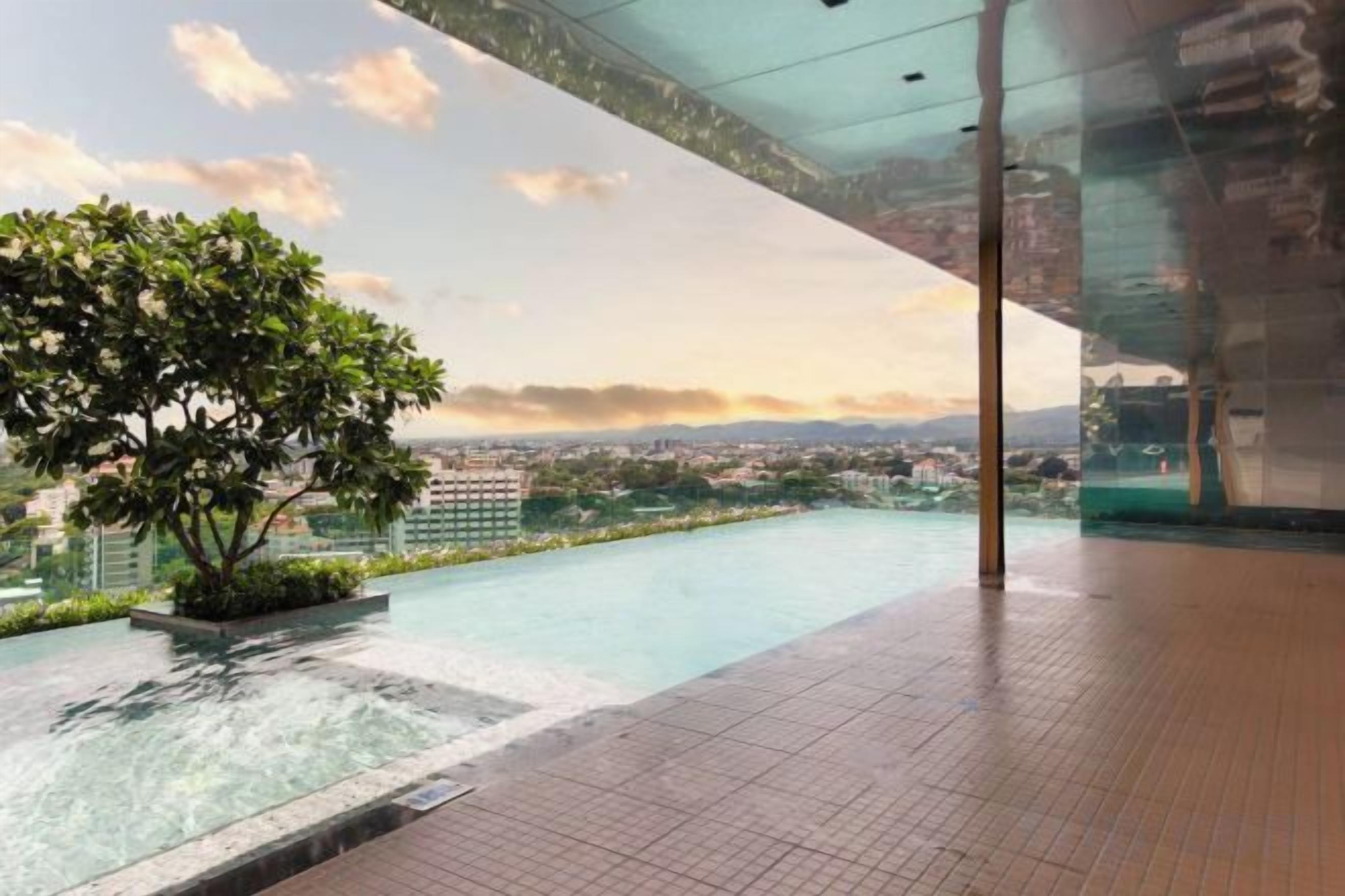 Una piscina en la azotea con vistas despejadas al paisaje urbano, rodeada de paredes de vidrio y un árbol en maceta.