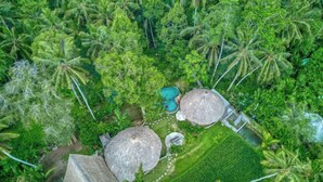 Eine Vogelperspektive eines tropischen Resorts mit strohgedeckten Hütten, einem Swimmingpool und üppiger Vegetation.