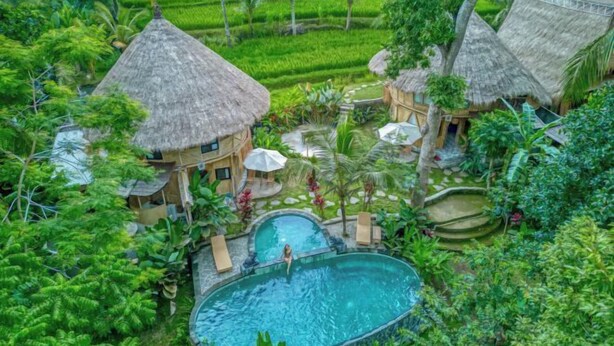 Ein tropisches Resort mit strohgedeckten Hütten, einem Schwimmbad und üppiger Vegetation.
