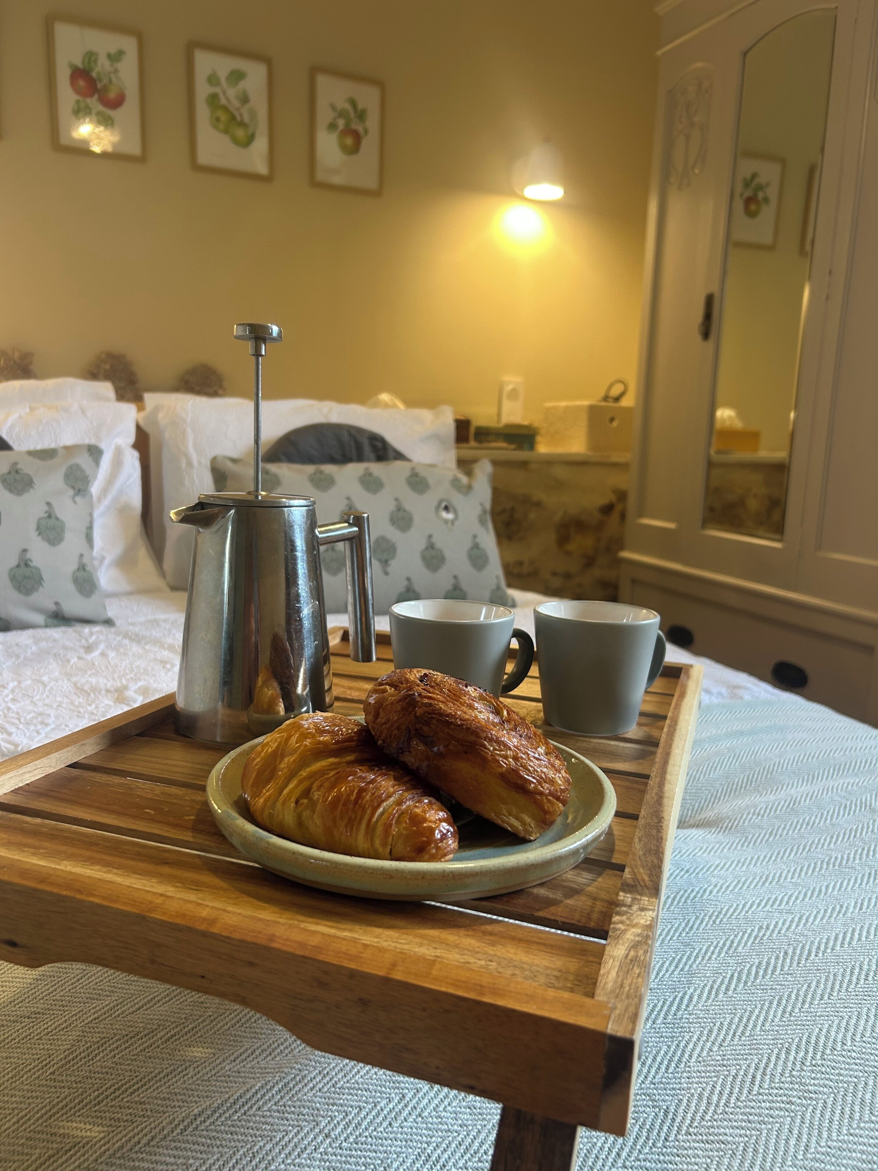 Ein Tablett mit Croissants, einer Kaffeekanne und einer Tasse auf einem Holztisch in einem Hotelzimmer.