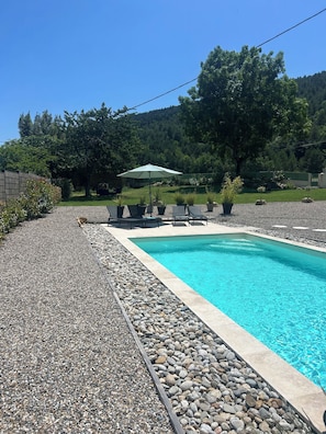 A swimming pool with a pebble border, surrounded by lounge chairs and an umbrella.