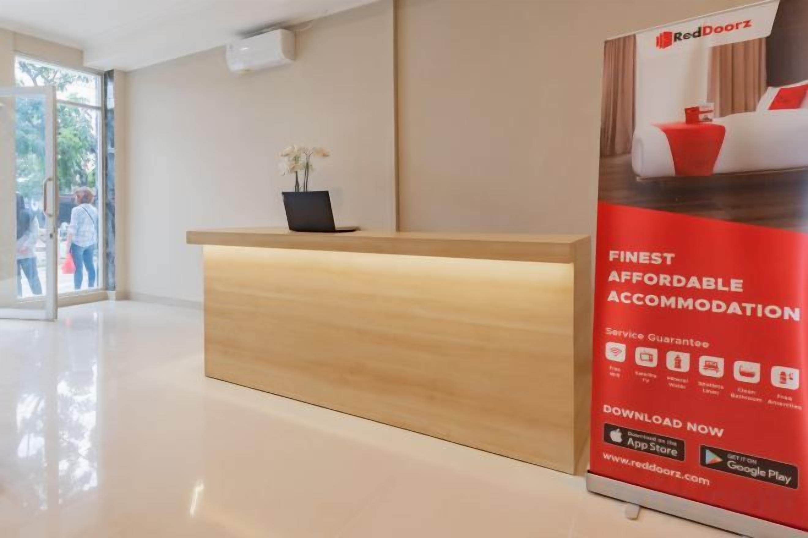 A hotel reception area with a wooden reception desk, a potted plant, and a poster advertising affordable accommodation.