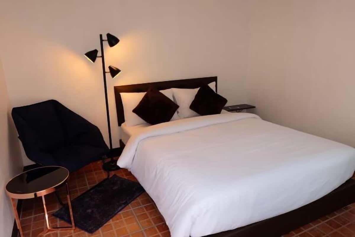 A neatly made bed with a dark headboard, a small round side table, and a floor lamp.