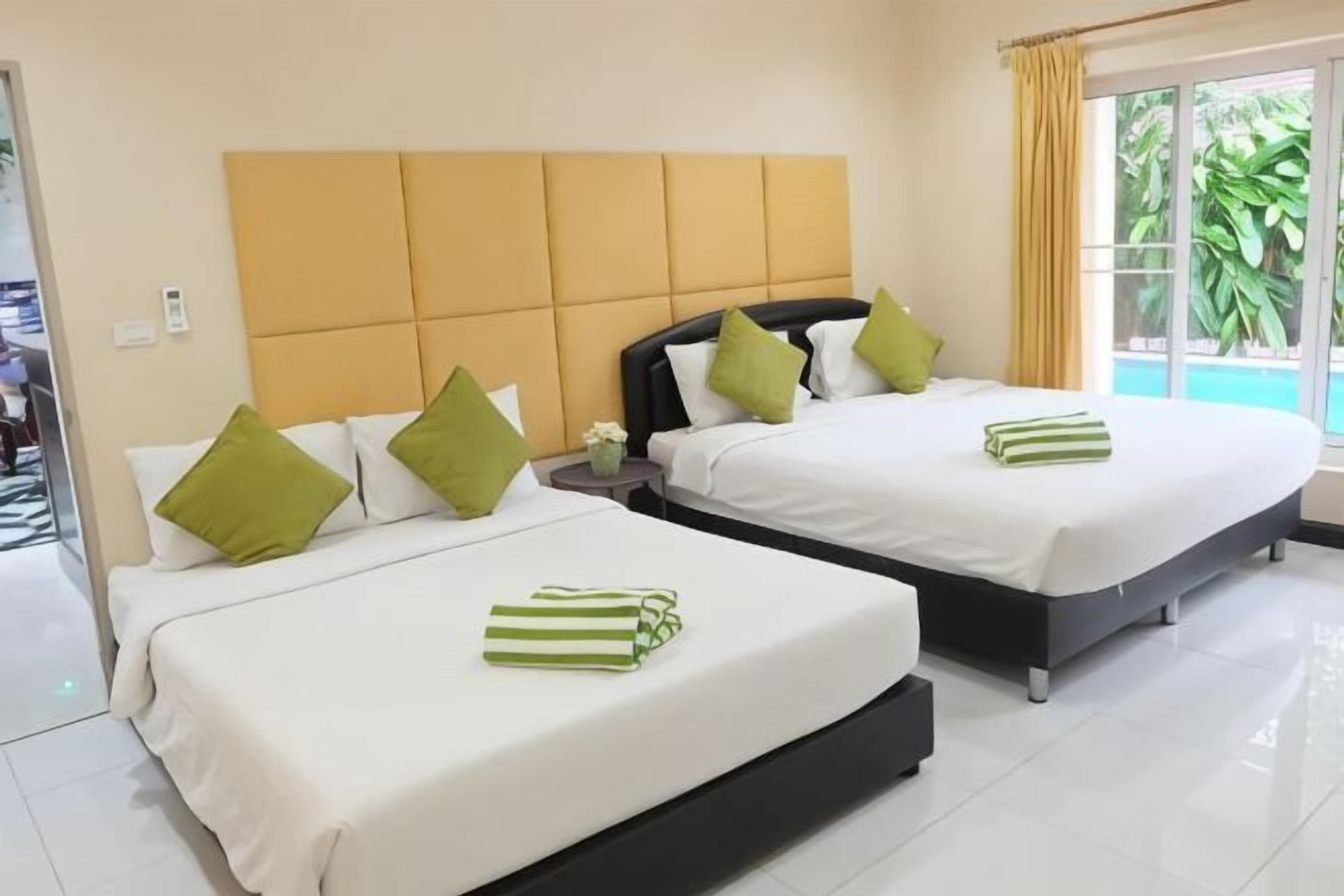 Duas camas com roupa de cama branca e almofadas verdes, uma cabeceira bege e uma janela com cortinas.