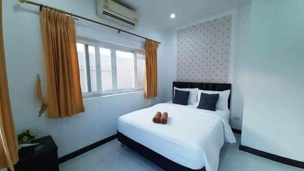 Una habitación de hotel con una cama grande, una ventana con cortinas, un equipo de aire acondicionado y una mesita de noche pequeña.
