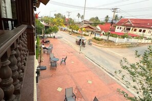 A street view with a building on the left, a paved area with tables and chairs, and a road with vehicles. - Heuangpaseuth Hotel (Luang Prabang)
