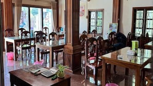 Egy hotel hallja, melyben fából készült bútorok, üveglapok és egy nagy ablak található.