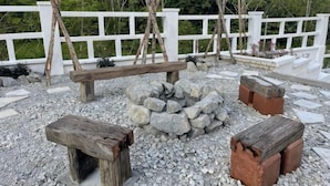 A rustic outdoor seating area with a stone fire pit, wooden benches, and a white fence. - Manson Goat Cottage (A) - Nature escape hideaway (Ulu Telom)
