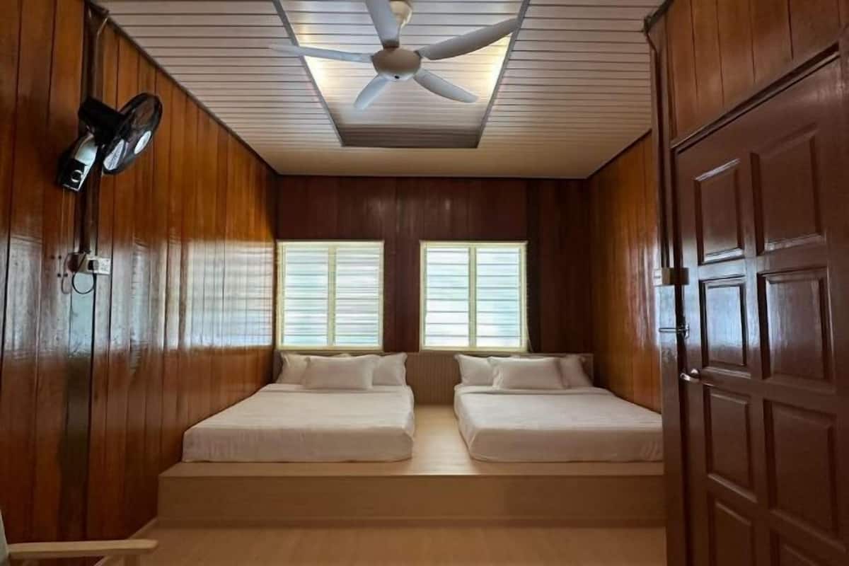 A room with two beds, a ceiling fan, and wooden walls.
