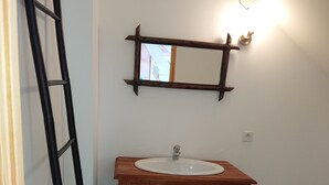 Ein Badezimmer mit einem Holzausziehtisch, einem weißen Waschbecken und einem Spiegel mit Holzrahmen.