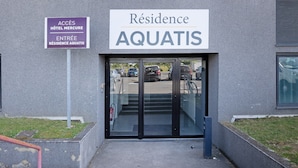 A building entrance with a sign reading 'Résidence AQUATIS' and another sign indicating 'ACCES HOTEL MERCURE' and 'ENTREE RÉSIDENCE AQUATIS'.